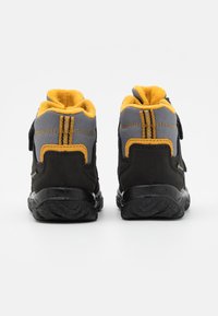 Scarpe da trekking nere e grigie con accenti gialli, dotate di una morbida fodera, suole in gomma testurizzata e doppia cucitura gialla sul retro.