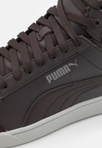 Brązowe skórzane trampki o teksturowanej powierzchni, z płaskimi sznurowadłami, białą gumową podeszwą i szarym logo Pumy po boku.