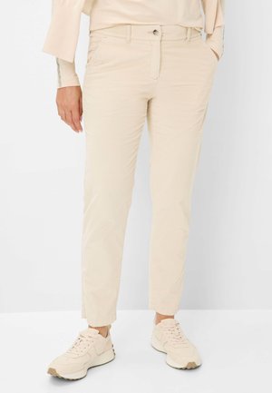 Beige Cordhosen mit geradem Schnitt, ausgestattet mit frontalen Taschen, einem Knopfverschluss und einer glatten Textur. Getragen mit hellen Sneakern.