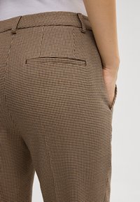 Pantalons à carreaux marron avec une coupe ajustée, comportant une poche arrière et une texture subtile dans un petit motif pied-de-poule.