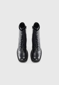 Schwarze Leder Schnürstiefeletten mit glatter Oberfläche, runden Zehen und einem seitlichen Reißverschluss. Mit farblich abgestimmtem Nähten und einem gepolsterten Schaft.