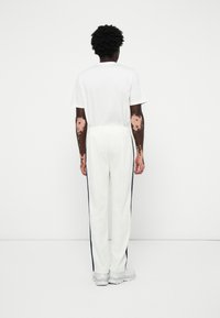 Camiseta blanca y pantalones de chándal blancos con rayas marinas laterales, cintura elástica y un corte relajado. Zapatillas grises completan el conjunto.