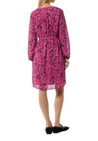 Rosa gemustertes Kleid mit langen Ärmeln, tailliertem Schnitt und lockerer Passform. Der Stoff ist leicht und leicht transparent, ergänzt durch schwarze Akzente.