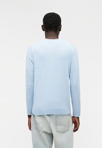 Pull bleu clair en tissu tricoté doux. Doté d'un col rond et d'un ourlet côtelé. Stylisé avec un jean bleu clair.