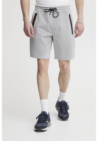 Shorts de sport gris avec une taille élastique, un cordon de serrage et des poches zippées noires. Portés avec des chaussures marines et des chaussettes blanches mi-mollet.