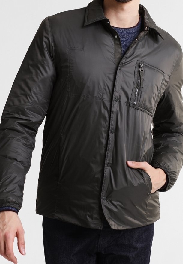 Chaqueta acolchada de color gris oscuro con un bolsillo en el pecho con cremallera, cuello de camisa, botones a presión y puños elásticos, hecha de material ligero.