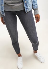 Jeans ajustados de mezclilla en gris oscuro, con una textura suave y un diseño ceñido, combinados con zapatillas blancas de velcro.