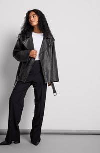 Schwarze Leder-Übergrößejacke mit großem Kragen, Reißverschlussdetails und lockerem Schnitt, kombiniert mit schwarzen weit geschnittenen Hosen und einem weißen Hemd.