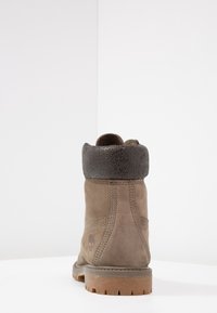 Bruine suède enkellaars met een gestructureerde zwarte boord, gestikte details en een rubberen zool met noppen voor grip. Timberland-logo zichtbaar.