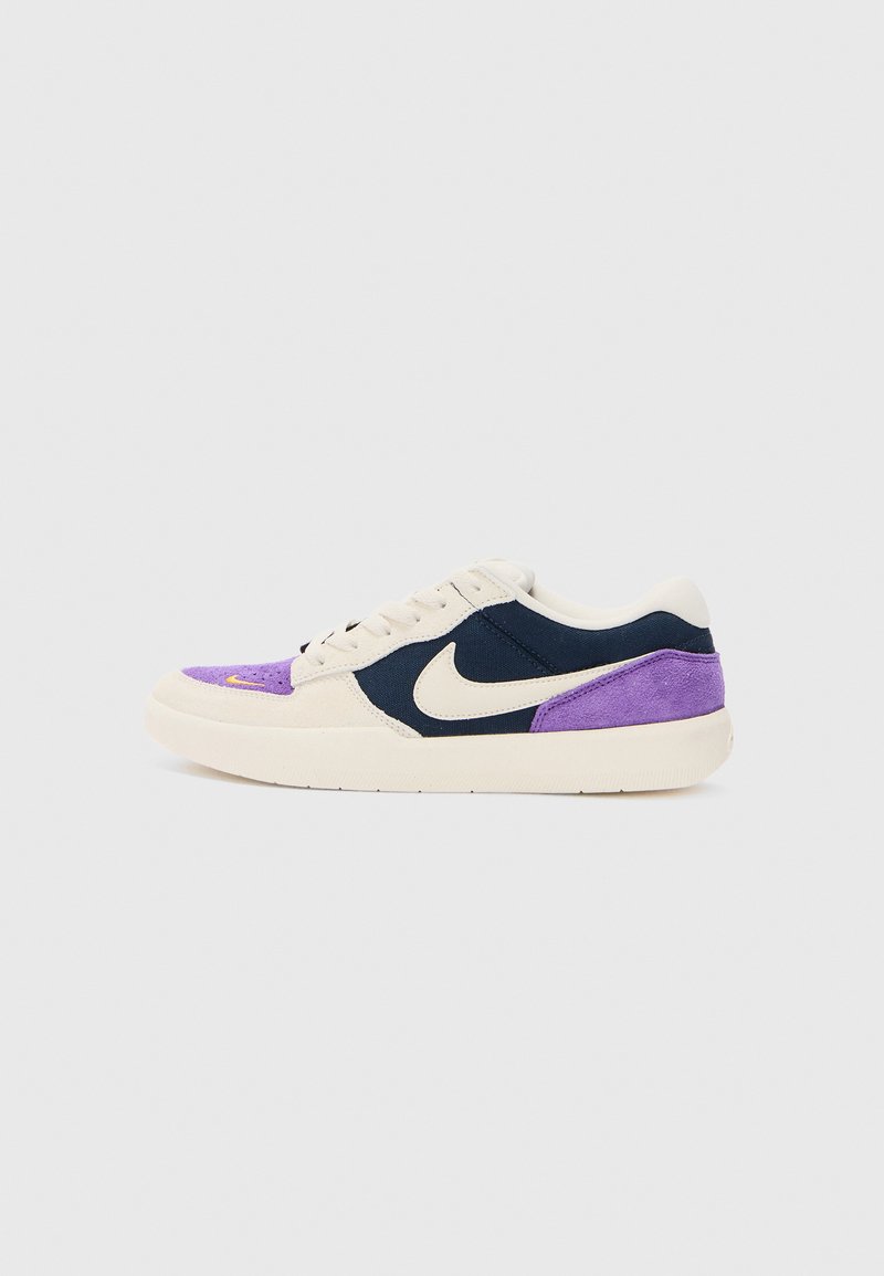 Baskets avec une tige crème, des accents bleu marine et un talon en daim violet. Le design inclut un swoosh Nike noir et une semelle en caoutchouc blanche.