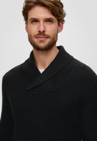 Zwarte gebreide trui met een chunky geribbelde textuur, voorzien van een brede sjaalkraag en een diep V-halsontwerp.