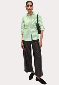 Groen-wit gestreepte overhemd met knopen en een borstzak, gecombineerd met zwarte leren wijde pantalon en zwarte instappers.