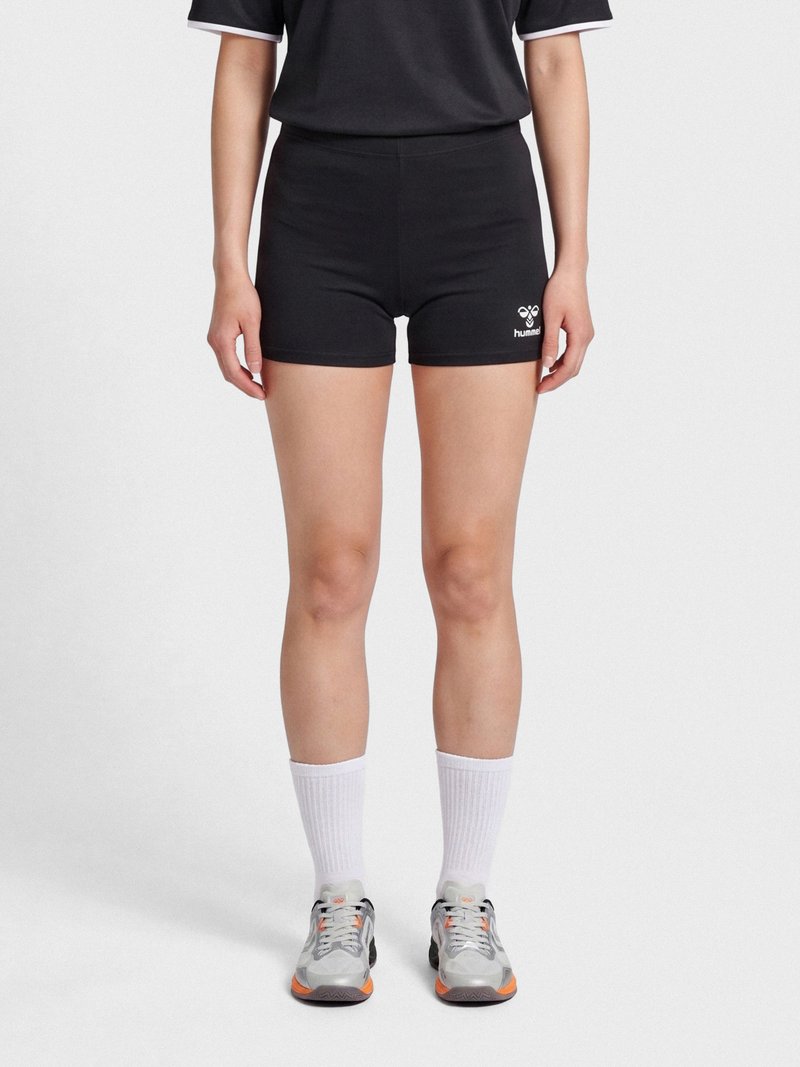 Person wearing black athletic shorts with a small white logo on the left thigh, white crew socks, and gray sneakers with orange accents.