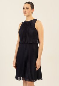 Ärmelloses, marineblaues, plissiertes Kleid mit tailliertem Oberteil und schwingendem Rock, das mit einem durchsichtigen Überzug und weichem Griff versehen ist.