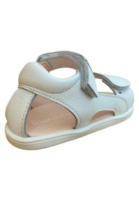 Sandalia de cuero blanco con diseño recortado, correa de Velcro, suela texturizada y forro interior suave para mayor comodidad.