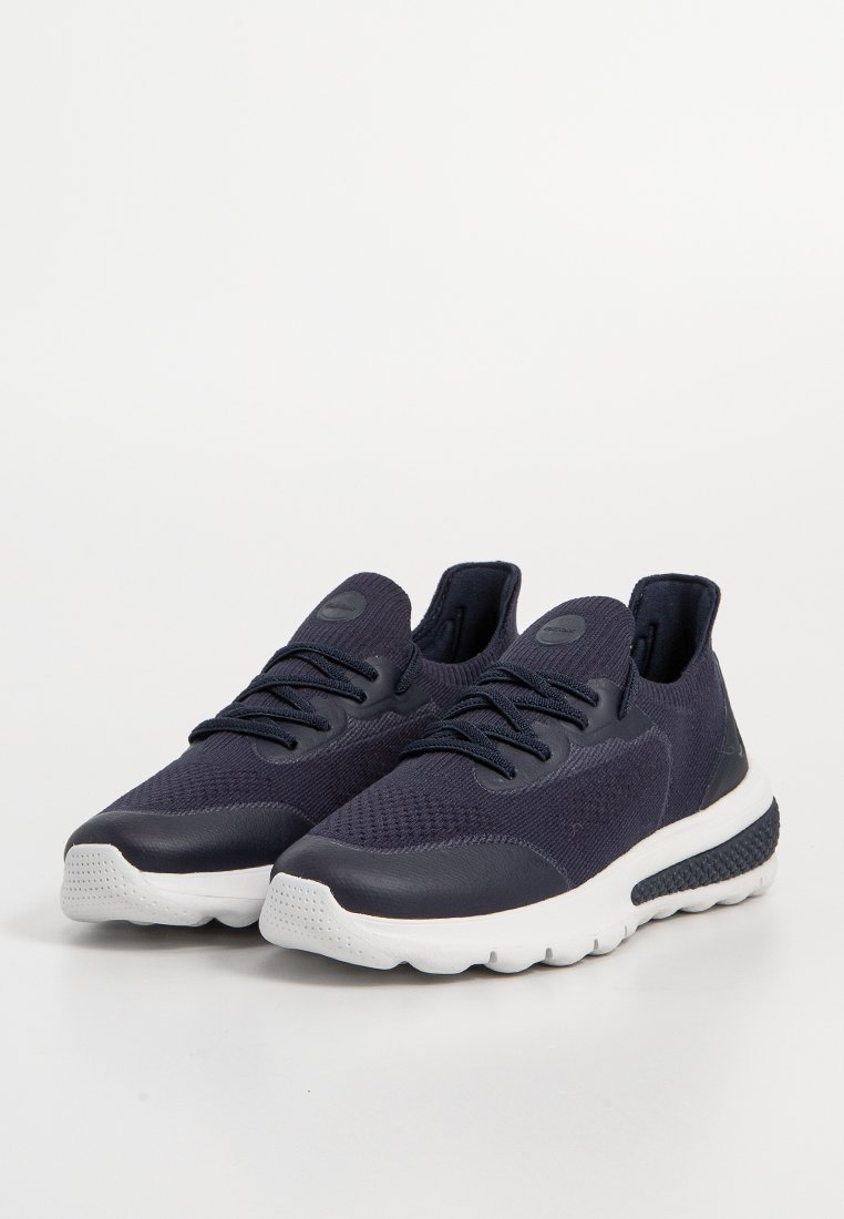 Baskets de sport bleu marine avec une tige en tissu texturé, dotées d'une semelle blanche, de lacets ronds et d'un ajustement serré autour de la cheville.