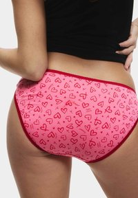 Rosa Baumwollslips mit roten Herzmustern, ausgestattet mit einem kontrastierenden roten Bund und Nähten. Sitzt eng anliegend und zeigt eine glatte Textur.