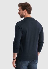 Langärmliges navyblaues T-Shirt aus weichem Stoff, mit rundem Halsausschnitt und eng anliegenden Ärmeln, kombiniert mit blauen Jeans.