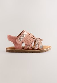 Sandalo in suede rosa con dettagli frangiati, intrecciati e cinturini metallici. Presenta una suola piatta con piccoli ritagli per la presa.