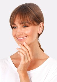 Anillo de oro con un diseño trenzado y texturizado en una mano reposando cerca de la cara. El modelo lleva una camisa blanca, tiene la piel suave y el cabello lacio y castaño.