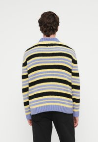 Pull en tricot rayé aux couleurs jaune, noir et lavande ; avec un ourlet et un col côtelés ; conçu avec une coupe décontractée.