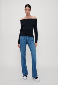 Svart ribbet off-the-shoulder topp kombinert med blå rettbente jeans. Fottøyet består av svarte lerrets sneakers med hvite såler og detaljer.