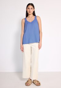 Top blu senza maniche con spalline arricciate, abbinato a pantaloni a gamba larga color crema e sandali beige. Tessuto morbido con una vestibilità rilassata.