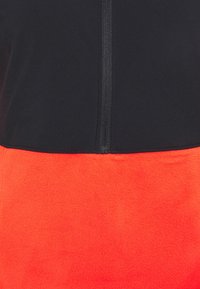 Pullover in pile con parte superiore nera e sezione inferiore rossa brillante. Presenta una zip frontale e una finitura morbida e textured.