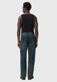 Jeans verde scuro a vestibilità ampia con gamba dritta, dotati di tasche posteriori e di un top nero senza maniche. Il tessuto presenta una texture sbiadita.