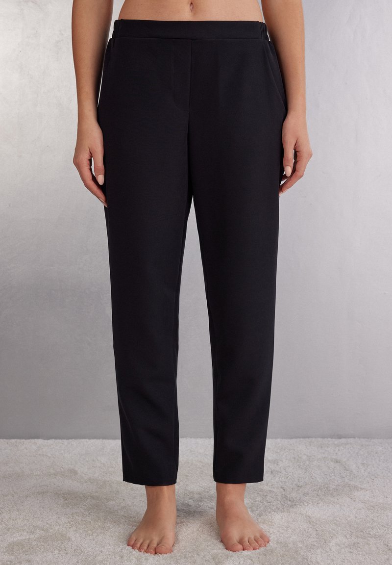 Pantaloni neri su misura con vita piatta e tasche laterali. Materiale liscio, vestibilità slim e design a gamba affusolata. Nessun motivo o accessorio visibile.