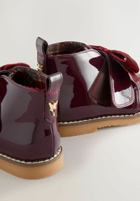 Bordeauxfarbene Lackleder-Stiefeletten mit einem strukturierten weinroten Einsatz und Schleifenakzent; goldfarbene Hardware-Details; Gummisohle.