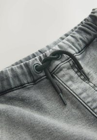 Pantaloni scurți din denim gri cu talie reglabilă prin șnur, având un șnur negru și elemente metalice pentru ochiuri; textură și detalii vizibile ale materialului.