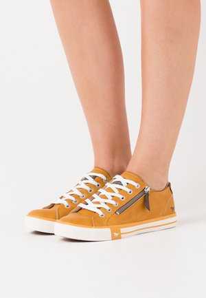 Schnürsneaker aus senfgelbem Leder, mit weißen Schnürsenkeln, einem Reißverschlussakzent an der Seite und einer weißen Gummisohle.