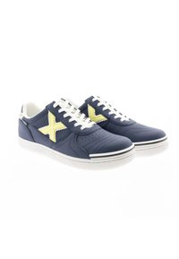 Zapatillas de deporte azul marino con detalles amarillos, parte superior texturizada, cordones blancos, lados perforados, suela de goma y ribete blanco en contraste.