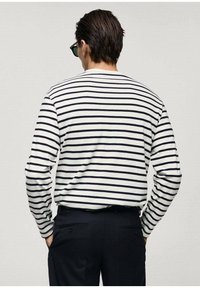 Camicia a maniche lunghe a righe in bianco e blu navy, con colletto rotondo e vestibilità comoda. Indossata con pantaloni scuri, che mostrano la vista posteriore.