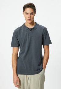Dunkelgraues Poloshirt mit kragenförmigem Halsauschnitt, einer Dreiknopf-Leiste und kurzen Ärmeln, aus weichem Material und mit lässigem Schnitt.