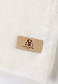 Tessuto a maglia color crema con una texture morbida e un'etichetta in pelle marrone che riporta la scritta "BELLEMERE NEW YORK," attaccata con due punti.