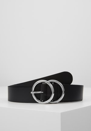 Black leather belt with double silver round metal buckle resting coiled on a white surface against a gray background.