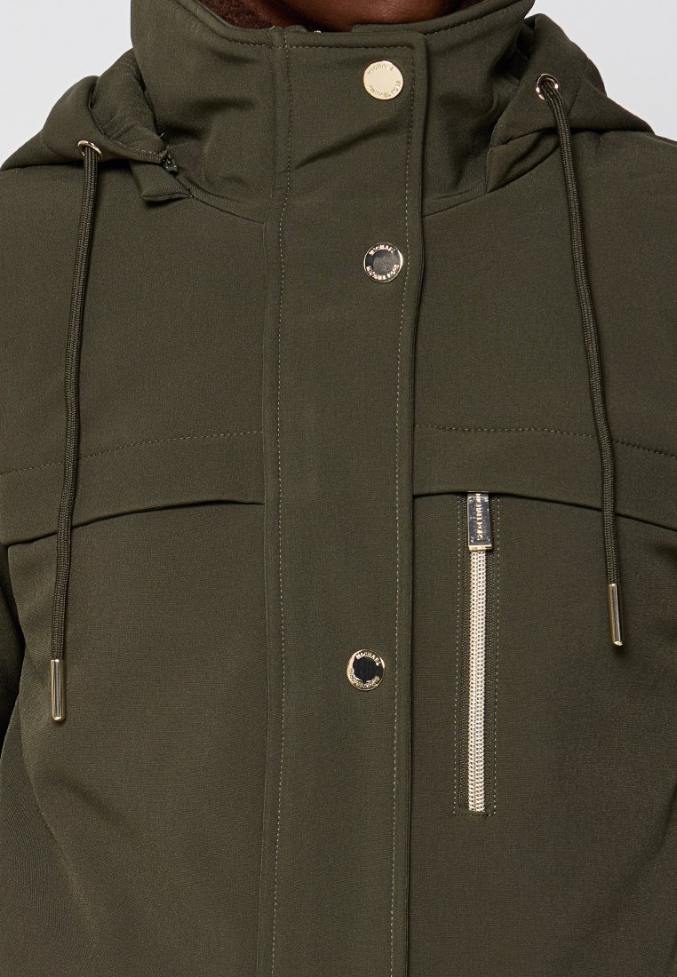 Giacca verde oliva con colletto alto, cordini regolabili, finiture dorate, tasche frontali e tasca laterale con zip.