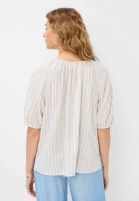 Lys beige kortærmet bluse med vertikale hvide striber, samlet halsudskæring og detalje med plissering bagpå. Blød stof med en afslappet pasform.