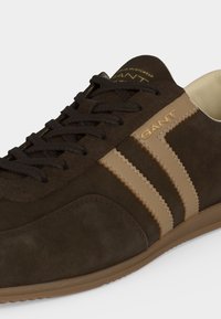 Καφέ sneaker από σουέντ με μπεζ ρίγες και καφέ κορδόνια, με το λογότυπο «GANT» στο πλάι και στη γλώσσα, και ανοιχτό καφέ σόλα.