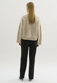 Beżowy, puszysty sweter o oversize'owym kroju i opadających ramionach, zestawiony z czarnymi spodniami o prostym kroju. Gładka faktura materiału, minimalistyczny design.