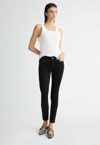 Jean skinny noir avec un design à cinq poches et des coutures subtiles, associé à un débardeur à côtes blanc et des ballerines noires ornées.