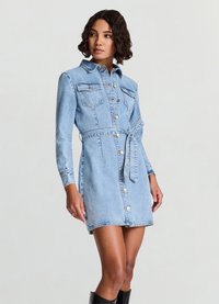 Jeanshemdkleid in Hellblau, mit langen Ärmeln, Brusttaschen, tailliertem Gürtel und Knopfverschluss. Glatte Textur mit leichter Used-Optik.