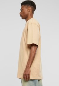 Přesně padnoucí oversized tričko vyrobené z bavlny, s krátkými rukávy, kulatým výstřihem a uvolněným střihem, předvedené na modelce z boku.