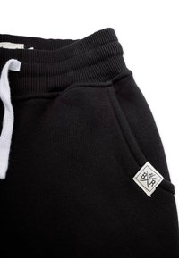 Sorte sweatpants med snøring i taljen, ribbede manchetter og et lille hvidt mærke med en diamantform på venstre side.
