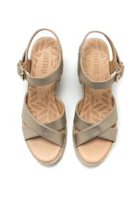 Sandales marron clair avec des brides croisées, boucle de cheville réglable et semelle intérieure texturée ornée de motifs de feuilles. Détail de semelle en jute. 