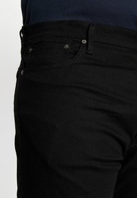 Vaqueros de algodón negro con ajuste slim, diseño de cinco bolsillos y acentos de botón metálico. Textura suave con un detalle de costura sutil.