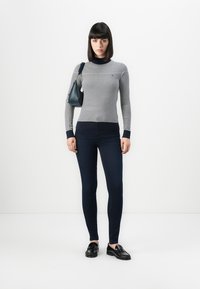 Stripet langermet topp i grått og marineblått, kombinert med mørkeblå skinny jeans. Tilbehøret inkluderer en liten marineblå håndveske og svarte loafers.