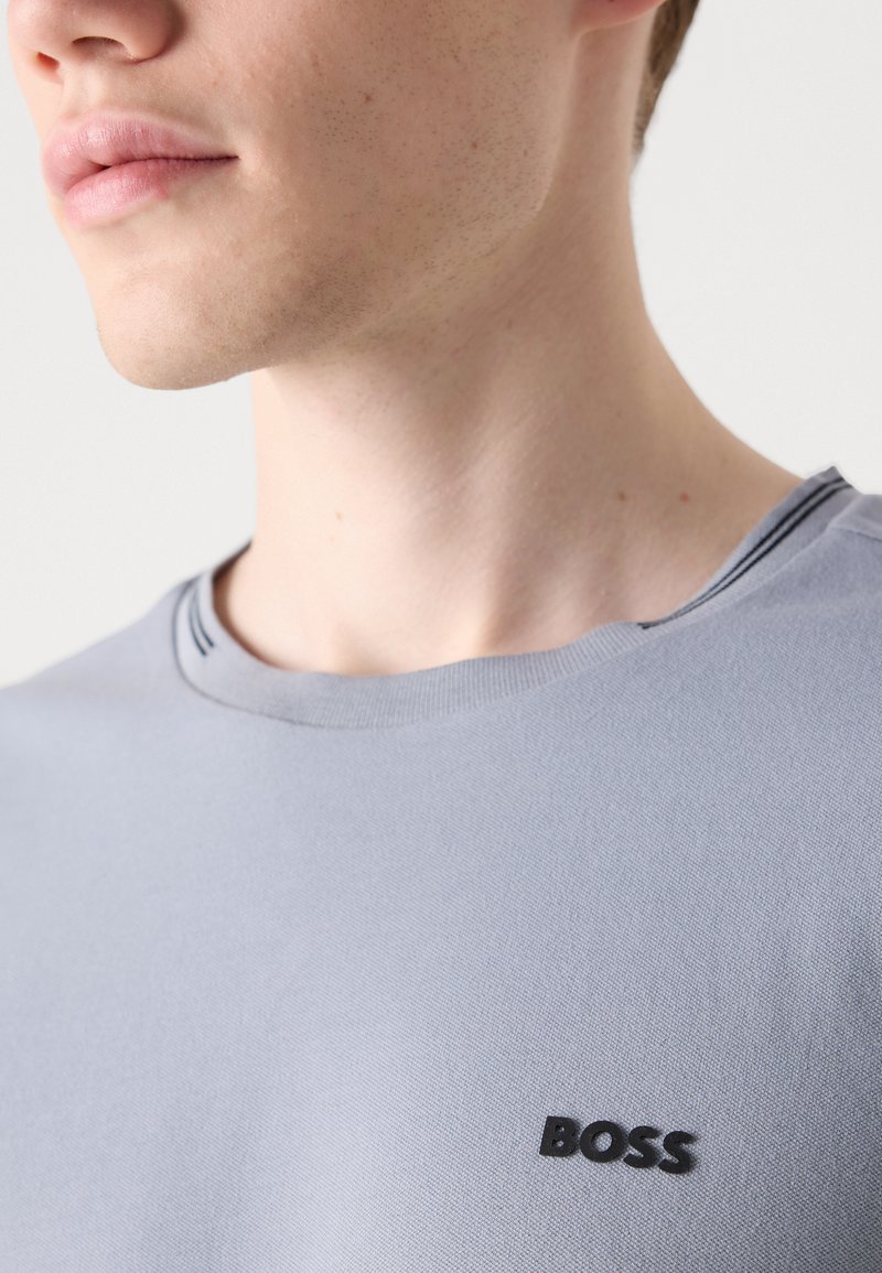 T-shirt gris clair à col rond en coton avec une texture lisse ; présente un petit logo noir "BOSS" sur la poitrine gauche.